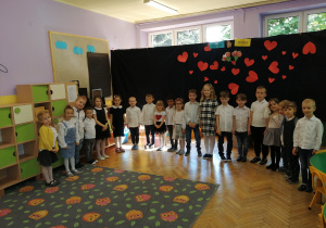 Zdjęcie dzieci z grupy fioletowej, dzieci stoją w kręgu z tyłu dekoracja z sercami dzieci ubrane są odświętnie
